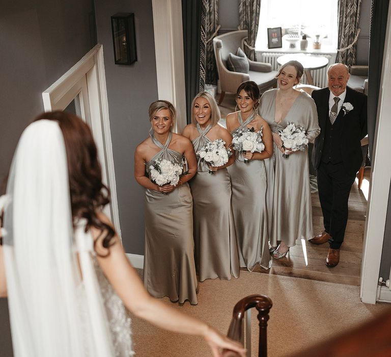 Bridesmaids and father of the bride get their first look at the bride in her wedding dress with the bridesmaids in sage green satin bridesmaid dresses 