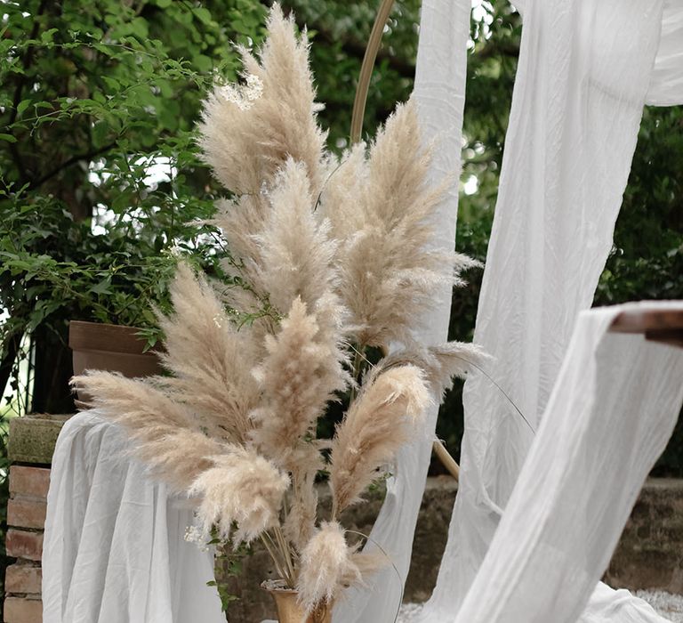 Large pampas grass installation outdoors beside white drapes and Moroccan styled rugs 