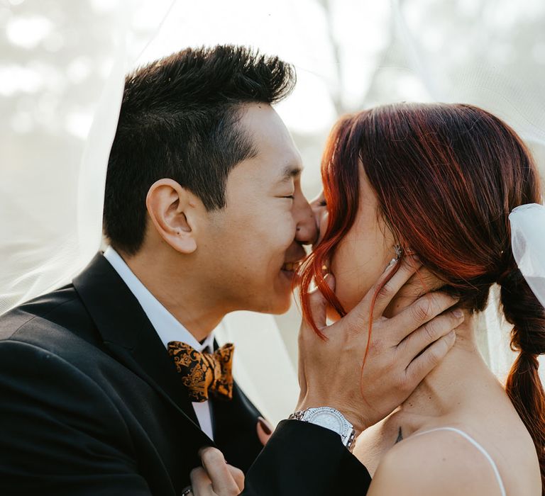 Groom kisses his bride beneath veil 