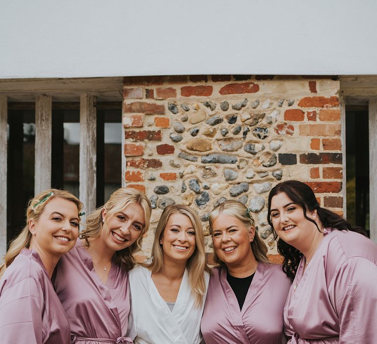 Bridal party with the bridesmaids in pink satin robes and bridesmaids in white satin robe as they all get ready for the wedding day 