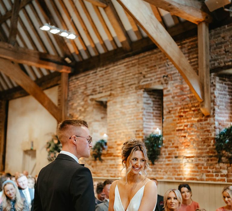 The bride with her hair in an updo holding hands with the groom for the civil ceremony at their black tie wedding 