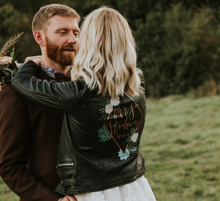 Personalised gold and rose wedding leather jacket in white wedding dress embracing the groom 