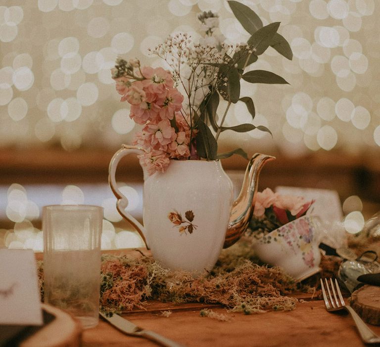 Antique teapots and teacups filled with pink flowers with moss acting as the table runner for outdoor boho wedding 