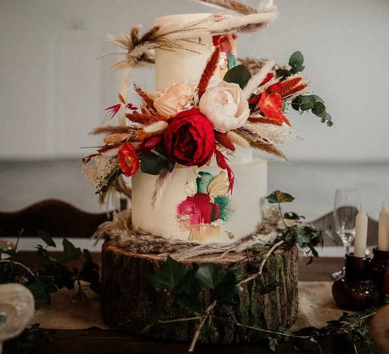 Three tier buttercream wedding cake with large decorative pampas grass, eucalyptus, dried flower and garden rose cake topper on large tree stump cake stand 