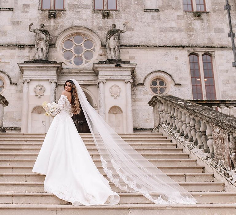 Bride in off the shoulder long sleeve sequinned Eva Lendel wedding dress walking the steps at Lulworth Castle 