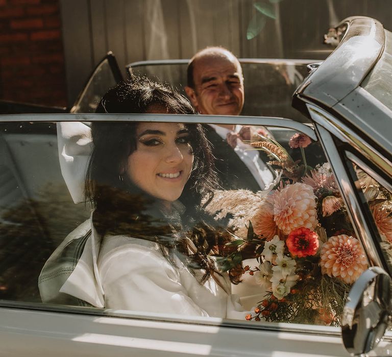 Bride in bouncy black hair tied with large white hair bow riding in the car with father of the bride 