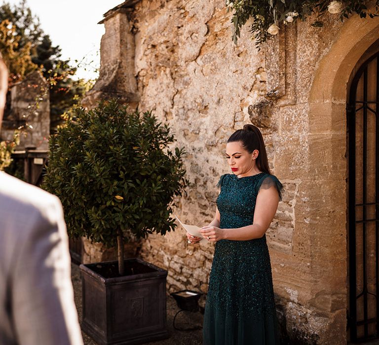 bridesmaid in dark green sparkly dress performing a wedding reading during the wedding ceremony 