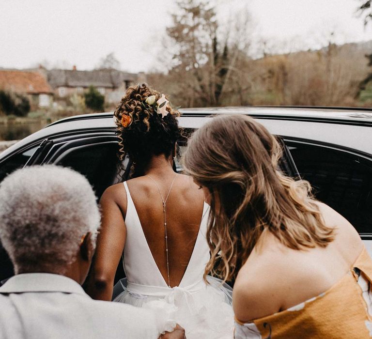 Bride in low back wedding dress with silver back chain wedding accessory getting into wedding car 