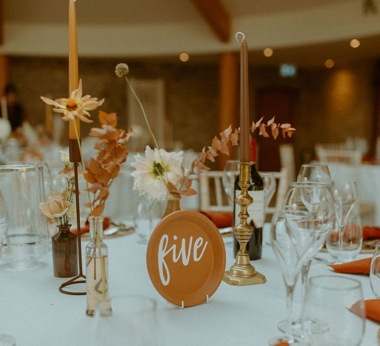 Table number sign on terracotta plate surrounded by taper candles and dried flower arrangements for boho wedding 