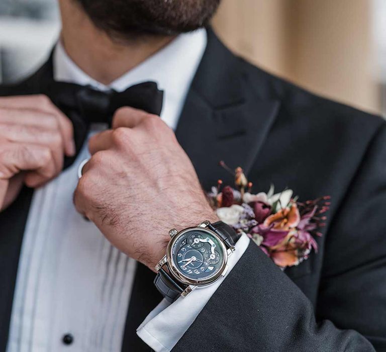 Stylish grooms accessories - Groom wearing gold and black watch, black bowtie, wildflower boutonniere and sleek classic black tuxedo