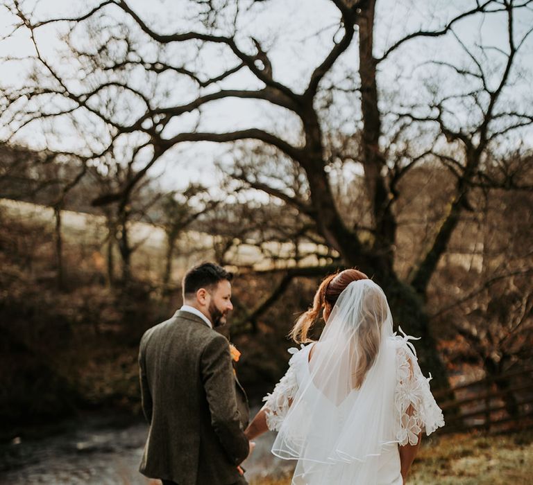 The bride wears a classic wedding veil walking around the venue grounds with the groom 