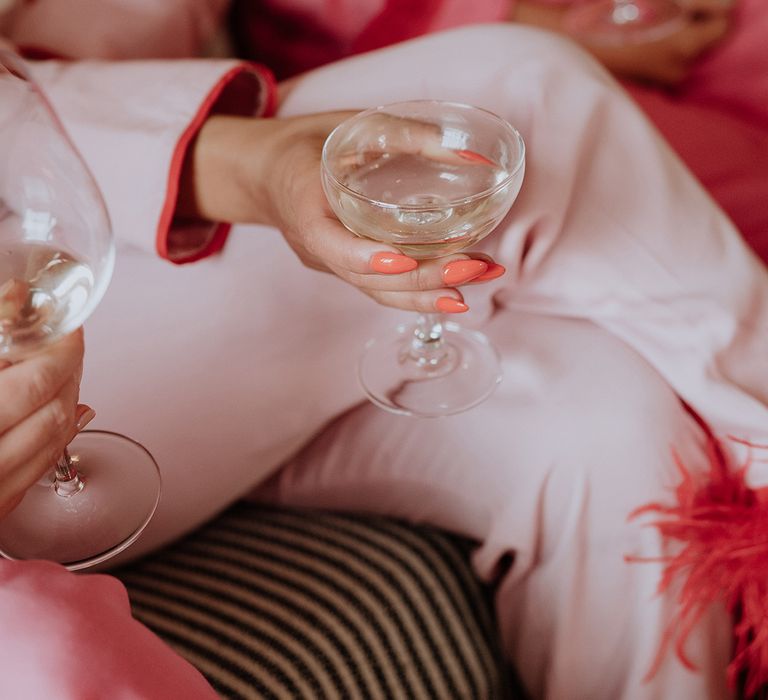 Bride with coral almond shaped wedding nails holding coupe glasses of champagne as they get ready 