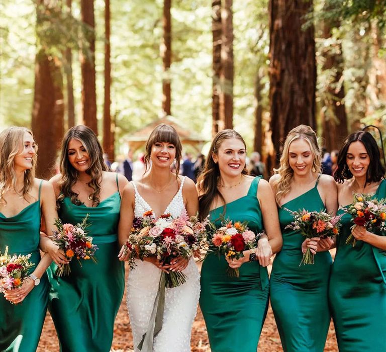 Bridesmaids in emerald green satin bridesmaid dresses with bride holding mini bouquets made from seasonal autumn wedding flowers 