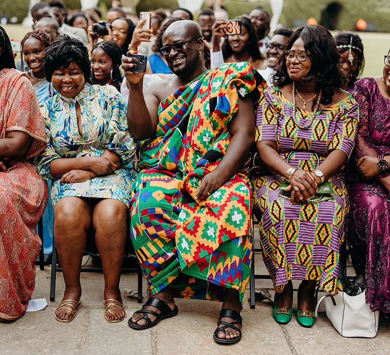 Front row of wedding guests in bright and colours wedding guest outfits for the outdoor multicultural wedding 