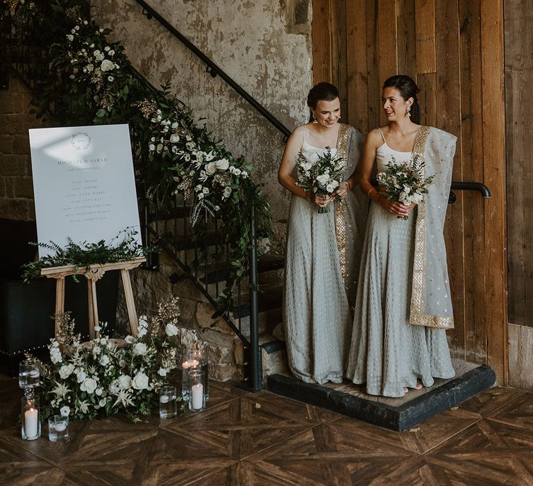 Bridesmaids in grey and gold saris for multicultural Indian English wedding next to minimalist wedding welcome sign 