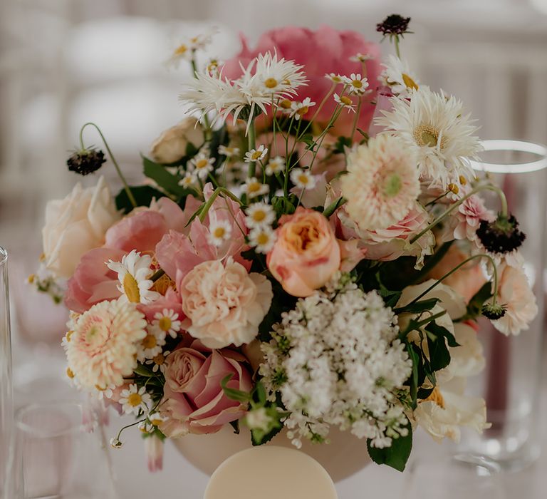 Flower table centrepiece featuring blush peonies, white daisies, gypsophila, and plush gerbera with blush and white acrylic table number