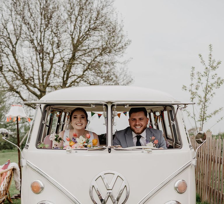 The bride and groom sit in the front seats of the VW campervan vintage wedding transport 