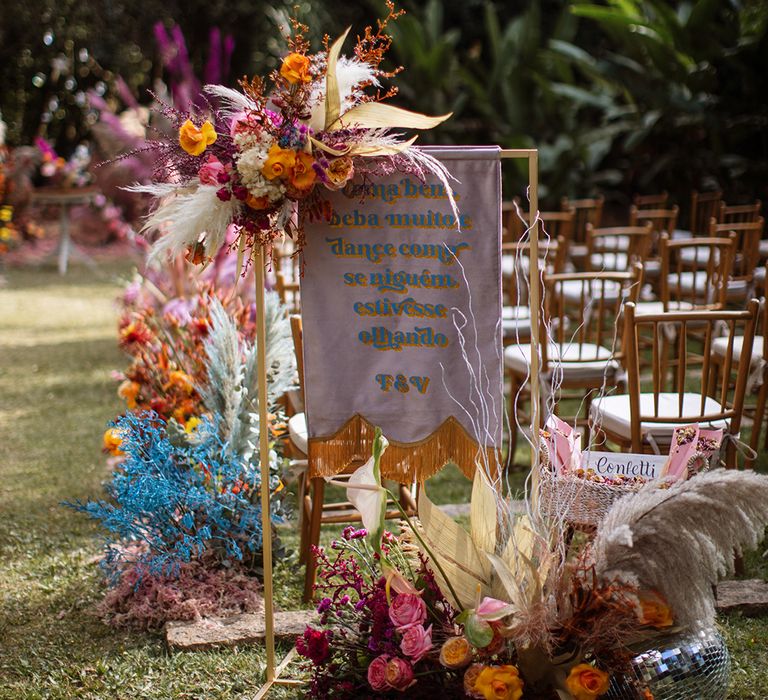 Bright and colourful wedding flowers with purple banner sign at the outdoor wedding ceremony 