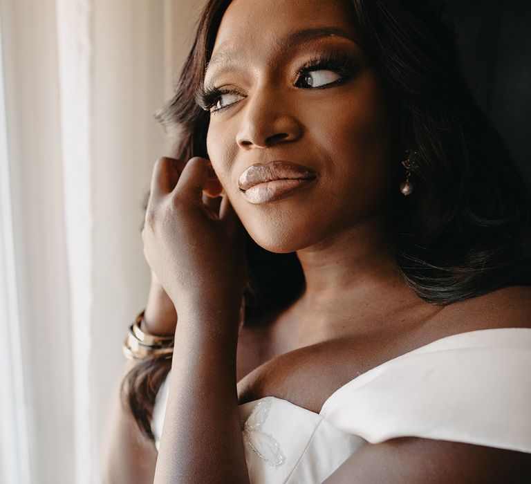 Bride in off the shoulder wedding dress putting on wedding earrings 