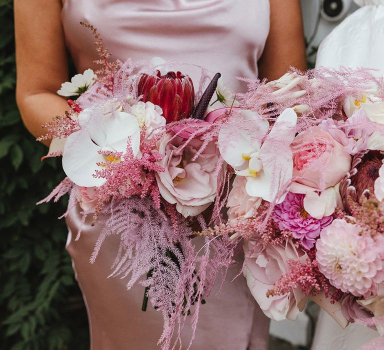 King proteas and orchids in this pink wedding bouquet held by bridesmaid in pink satin bridesmaid dress 