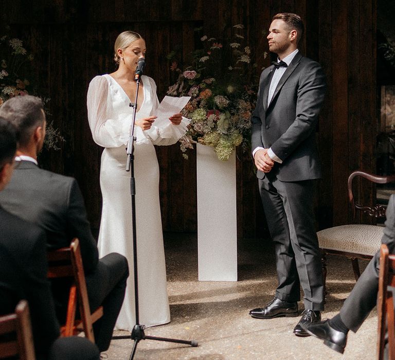 Bride wearing a wedding dress with sheer sleeves reading wedding vows at humanist ceremony 