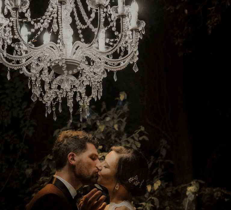 Bride and groom share a kiss under a stunning chandelier 