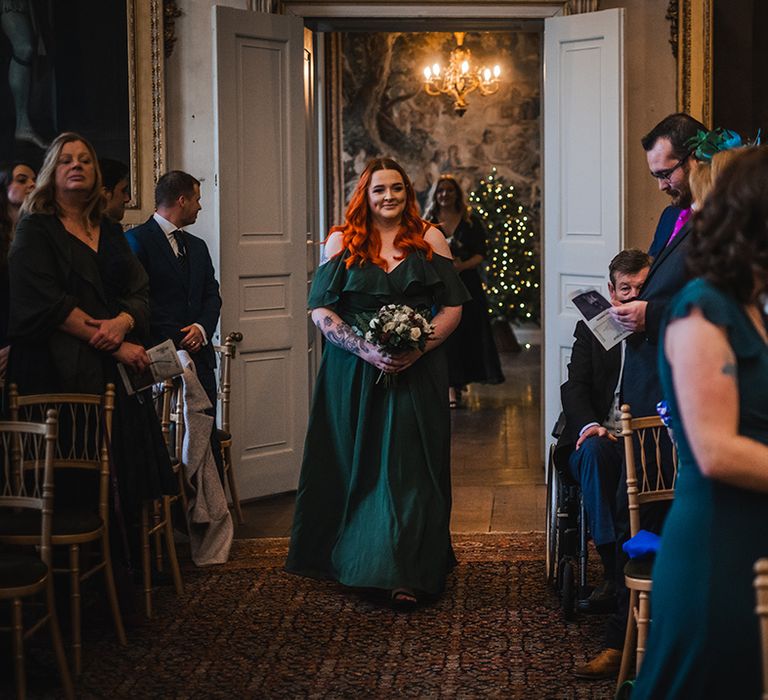 Bridesmaid walks down the aisle in an emerald green bridesmaid dress for Christmas wedding 