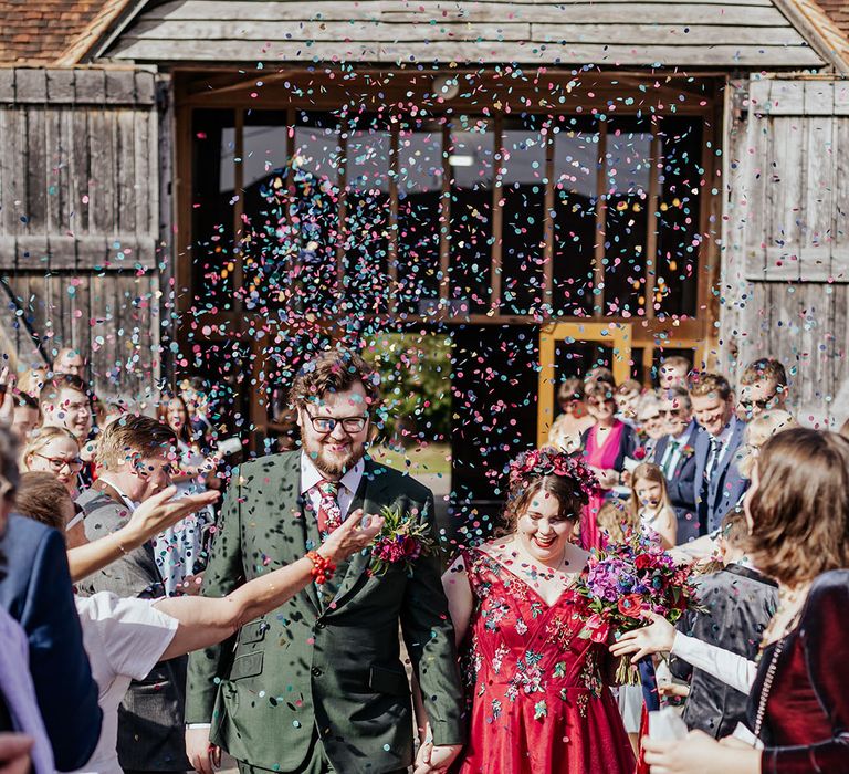 Colourful confetti moment at barn wedding with groom in forest green wedding suit with bride wearing red wedding dress 