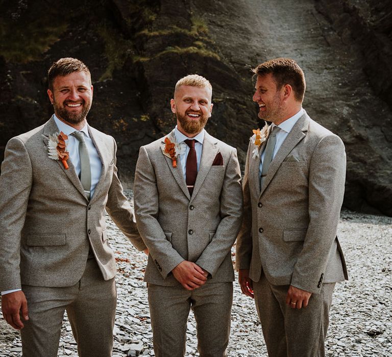 The groom and two groomsmen stand in matching suits together 