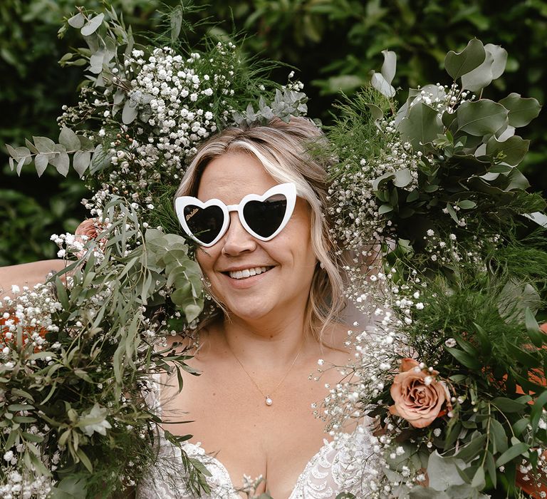 Bride wearing white retro sunglasses surrounded by white gypsophila and wedding flowers 