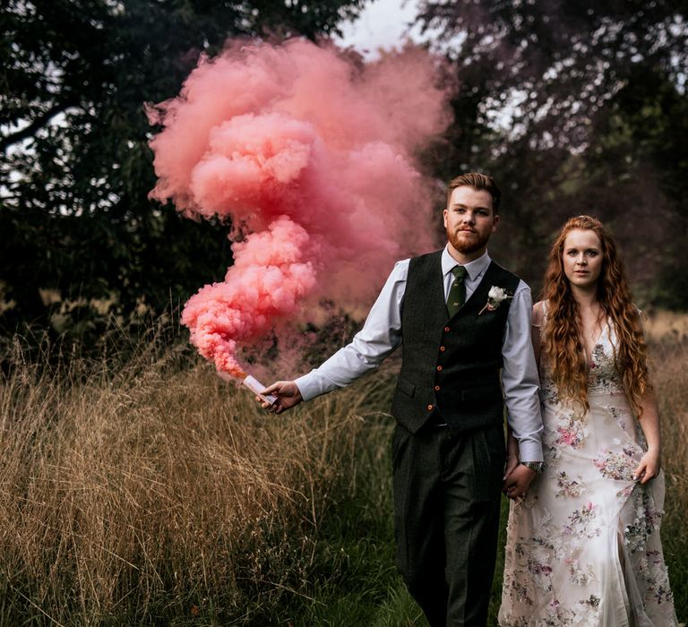 Bride & groom walk through the countryside with pink smoke bomb 