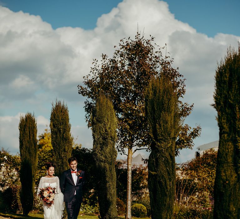 Bride & groom walk through grounds in the sunshine