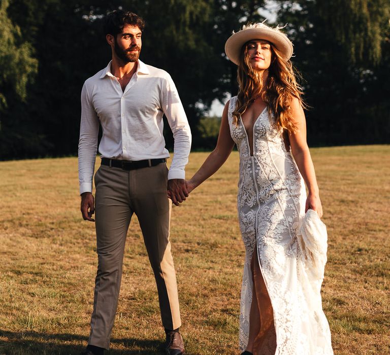 Bride and groom walk through fields together during golden hour