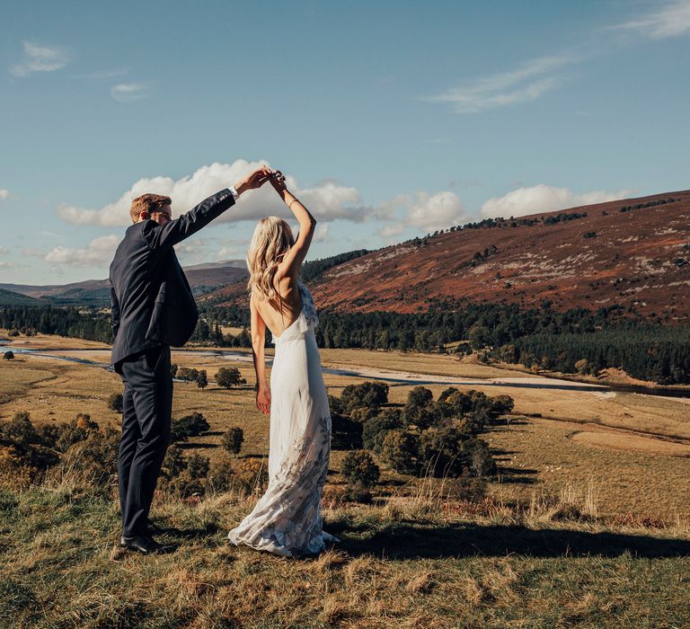 Groom twirls bride in the Scottish countryside with hills in the background