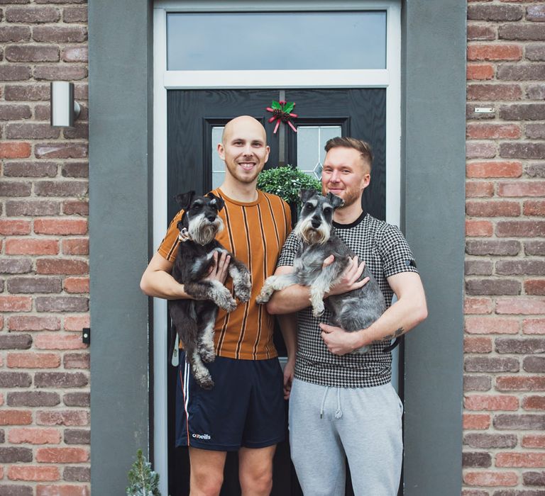 Two grooms standing outside their house with their pet dogs 