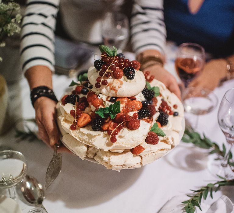 Three tier pavlova garnished with summer fruits being served at a table