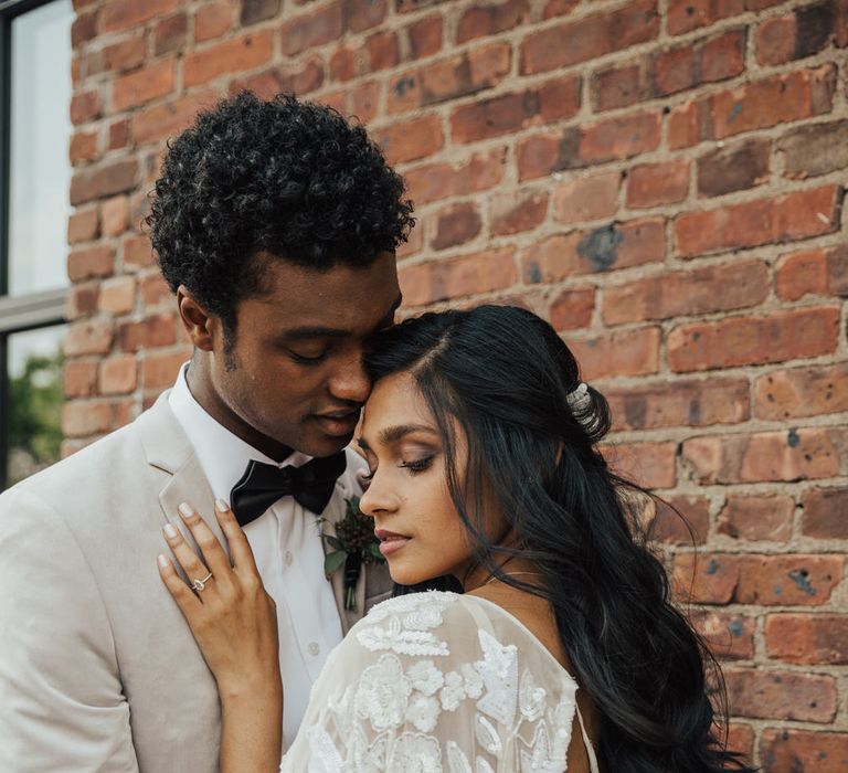 Asian bride with smokey eye makeup and sparkly wedding dress embracing her groom in a light grey jacket and bow tie 