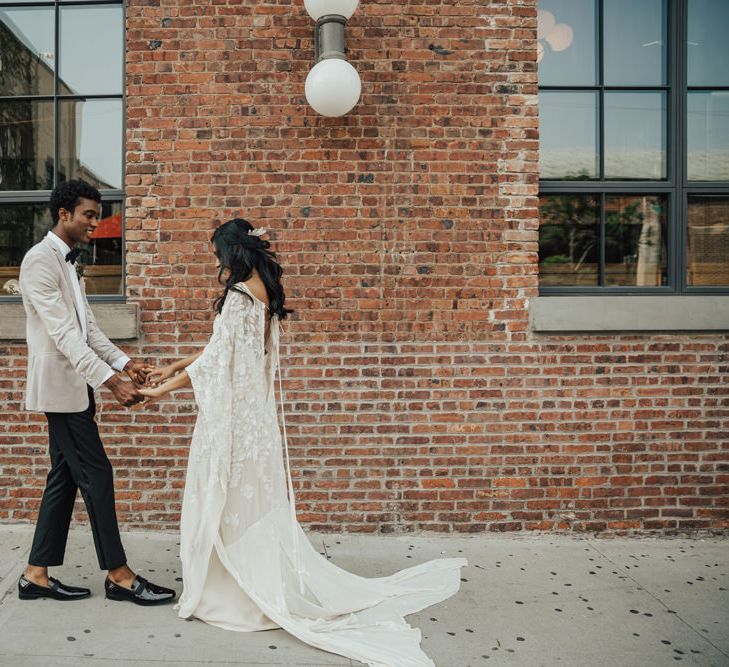 Bride and groom first look with groom in black trousers, patent shoes and grey blazer and bride in an embellished boho wedding dress 