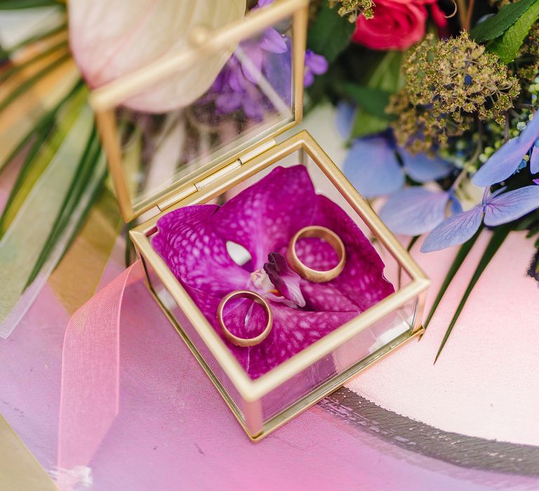 Gold wedding rings are placed in see through box with orchid pink flower