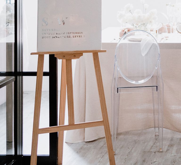 Minimalist wedding decor with white and silver foil welcome sign, ghost chairs and white flowers 