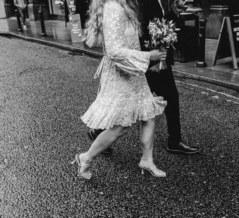 Black and white wedding photography pf bride and groom walking down the street, bride wears knee length floaty dress