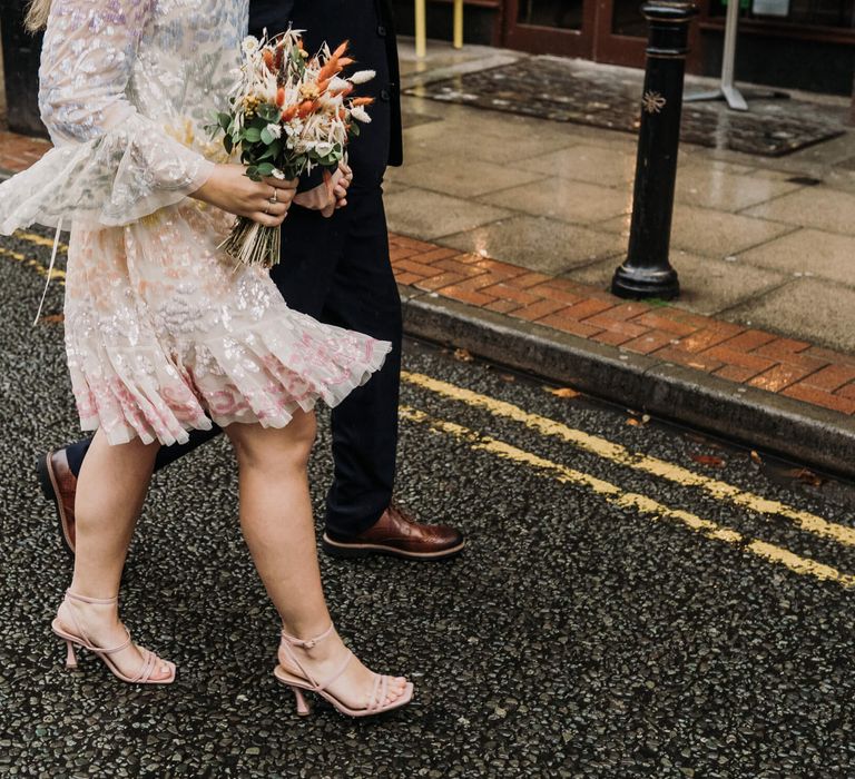 Bride walking down the street wearing pink heels and knee length pastel embellished wedding dress for Manchester wedding