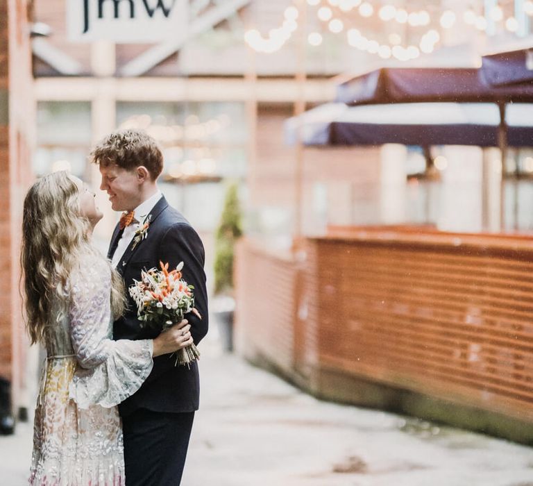 Bride and groom holding each other, bride wears pastel wedding dress and pink heels 