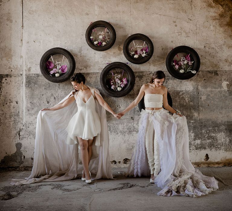 Two brides in a mini wedding dress and cape and bridal separates and detachable skirt standing in front of their tyre table plan 