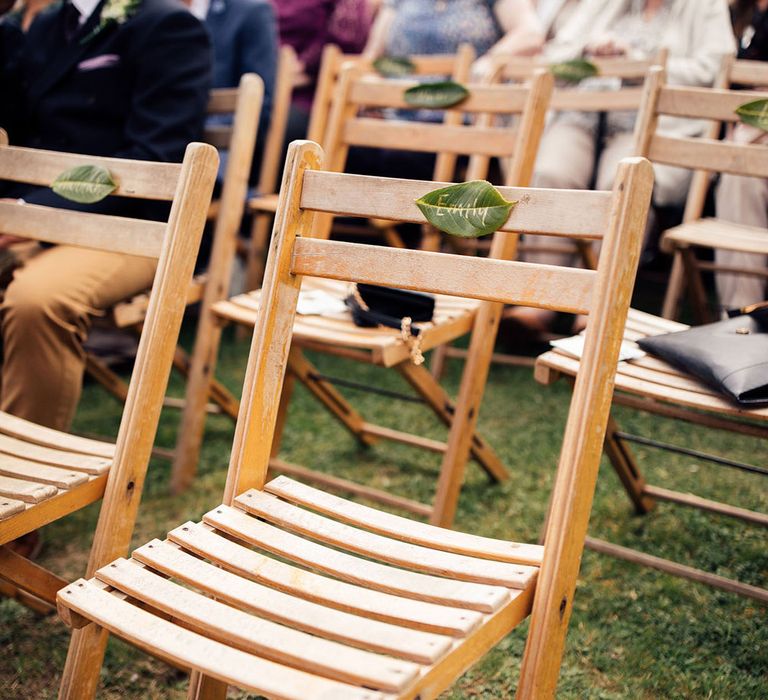 Wooden folding wedding chairs on grass with leaf name labels