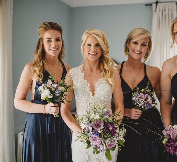 Three bridesmaids in multiway navy bridesmaid dresses holding purple and white bouquets including roses and thistles | Antonija Nekic Photography