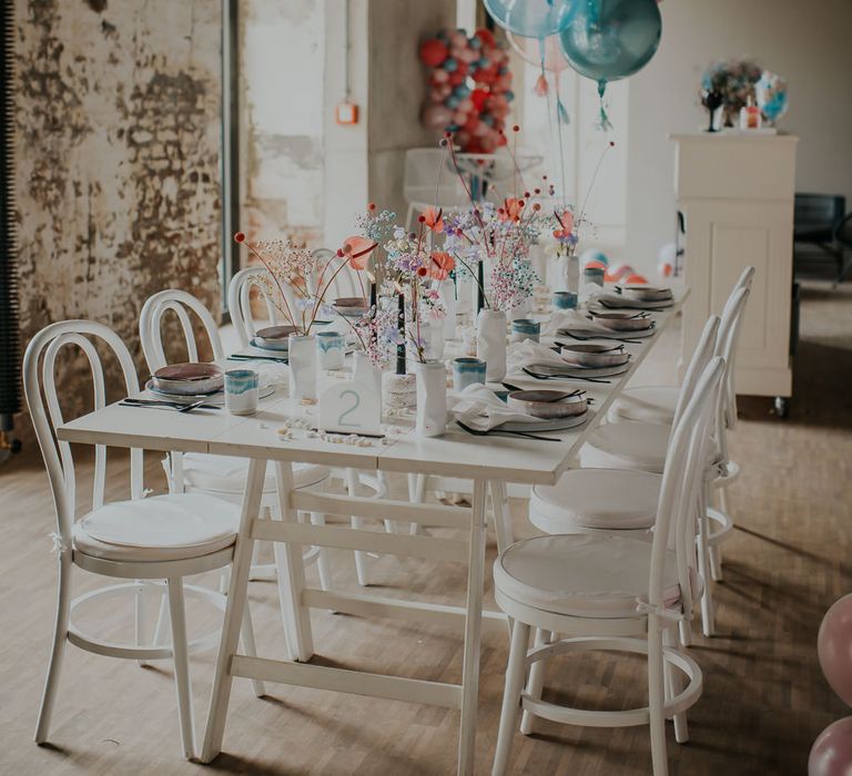 Intimate tablescape at Industrial wedding venue with white furniture and pastel flowers, balloons and decor. 