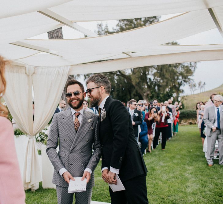 A gay couple laugh during their outdoor wedding ceremony. Photography by Deborah Lo Castro.