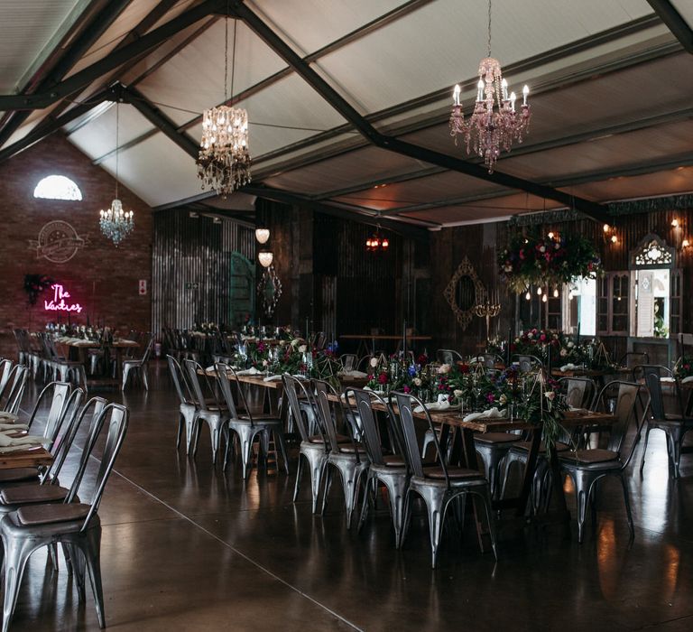 Rustic chic banquet table set up with moody romantic florals, foliage centrepieces and chandeliers