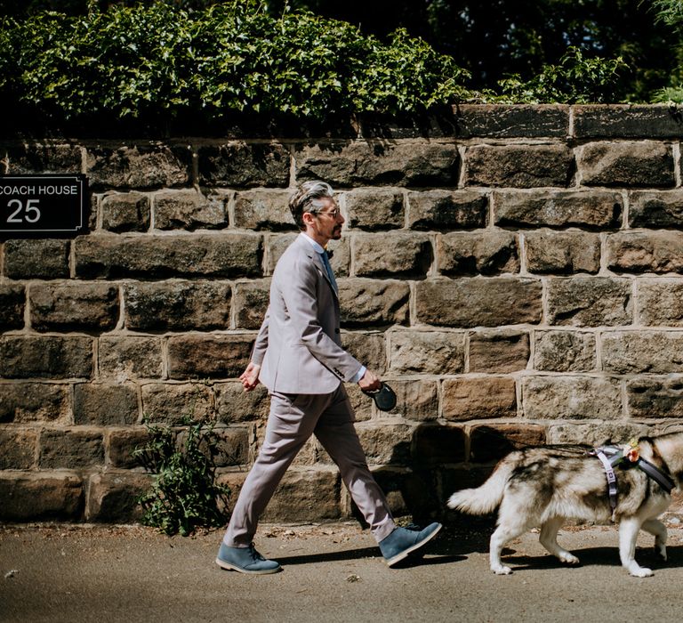 Groom in brown Moss Bros suit, blue tie and sunglasses walks through Harrogate with husky dog before Harrogate wedding